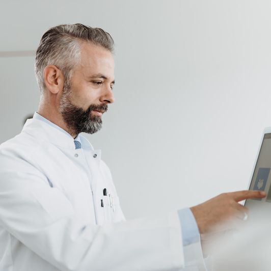 Facharzt für Psychiatrie und Psychotherapie Dr. Gjergji Sinani, Facharzt für Psychiatrie und Psychotherapie, in einem weißen Doktorkittel tippt auf einen Bildschirm