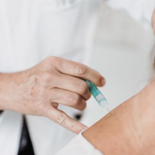 Einer Person wird von einem Arzt im Rahmen der Neuraltherapie ein Medikament in den Nacken gespritzt.
