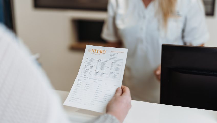 Eine Person blickt auf einen Termin-Zettel von NEURO Südwestfalen in der rechten Hand.