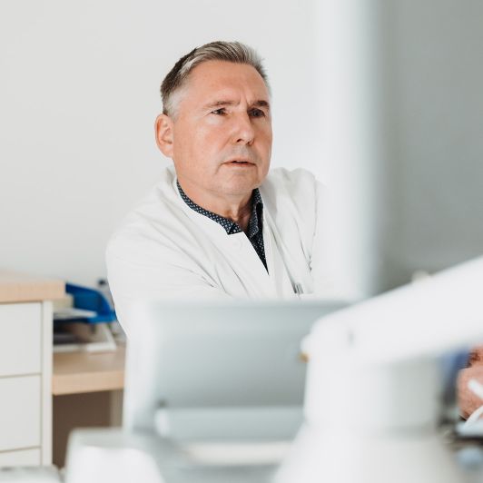 Lichttherapie bei NEURO Südwestfalen Georg Hübner im weißen Arztkittel, Facharzt für Neurologie und Nervenheilkunde in Siegen, blickt konzentriert auf einen Monitor