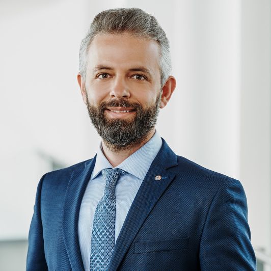 Portraitfoto von Dr. Gjergji Sinani, Facharzt für Psychiatrie und Psychotherapie. Er trägt einen dunkelblauen Anzug, ein hellblaues Hemd und eine blau gemusterte Krawatte. Er lächelt in die Kamera.