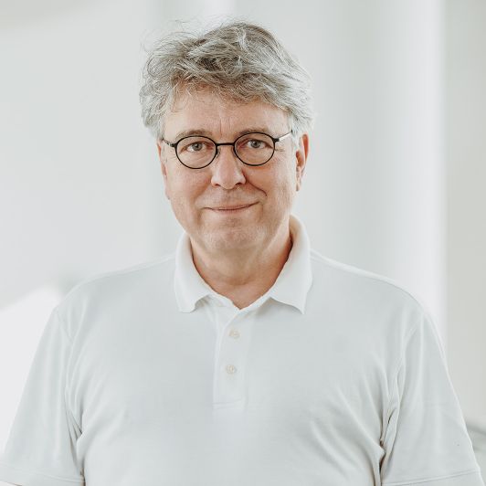 Portraitfoto von Dr. med. Jürgen Schulz, Facharzt für Neurologie und Psychiatrie. Er trägt ein weißes Polohemd und lächelt.