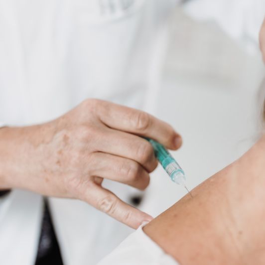 Eine Hand spritzt Procain zur Schmerzbehandlung und Neuraltherapie in den Nacken eines Patienten.