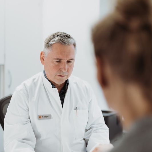 Georg Hübner im weißen Arztkittel, Facharzt für Neurologie und Nervenheilkunde in Siegen und Burbach, im Patientengespräch.