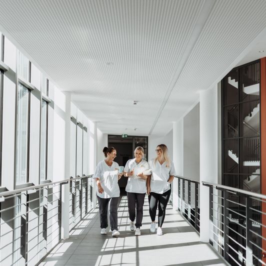 Neurologie, Psychiatrie und Psychotherapie in Siegen, Burbach und Bad Berleburg Drei lachende Mitarbeiterinnen in einem Gang des Albertus Magnus Zentrums in Siegen