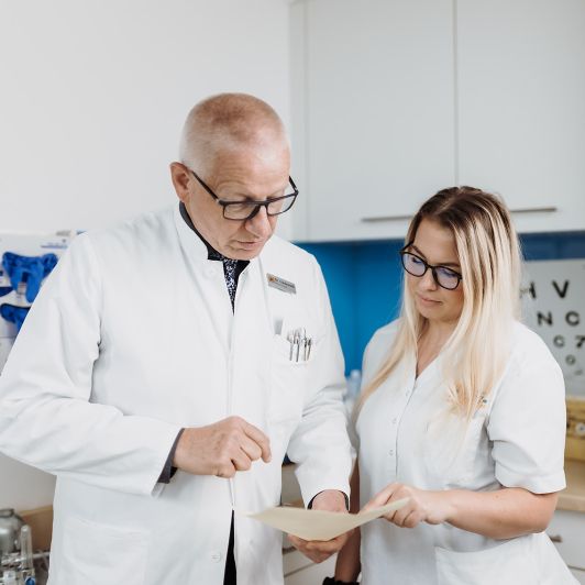 Dr. med. Rainer Lindemuth von NEURO Südwestfalen im weißen Kittel im Gespräch mit einer medizinischen Fachangestellten mit blonden Haaren und Brille.