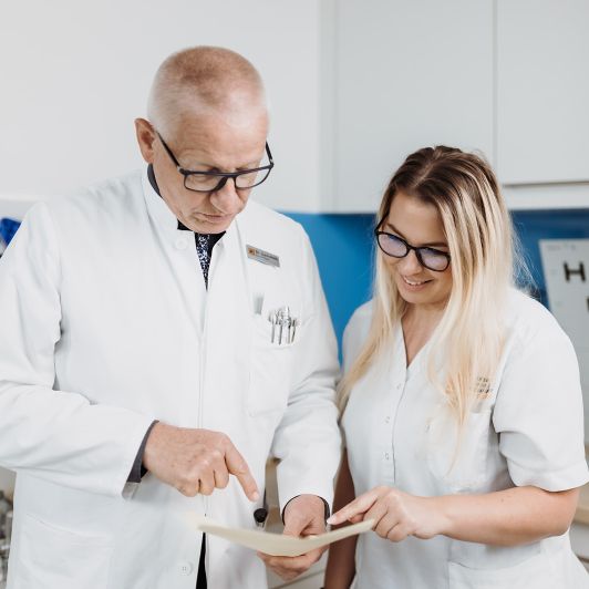 Neurologie, Psychiatrie und Psychotherapie in Siegen, Burbach und Bad Berleburg Dr. med. Rainer Lindemuth von NEURO Südwestfalen im weißen Kittel im Gespräch mit einer medizinischen Fachangestellten.