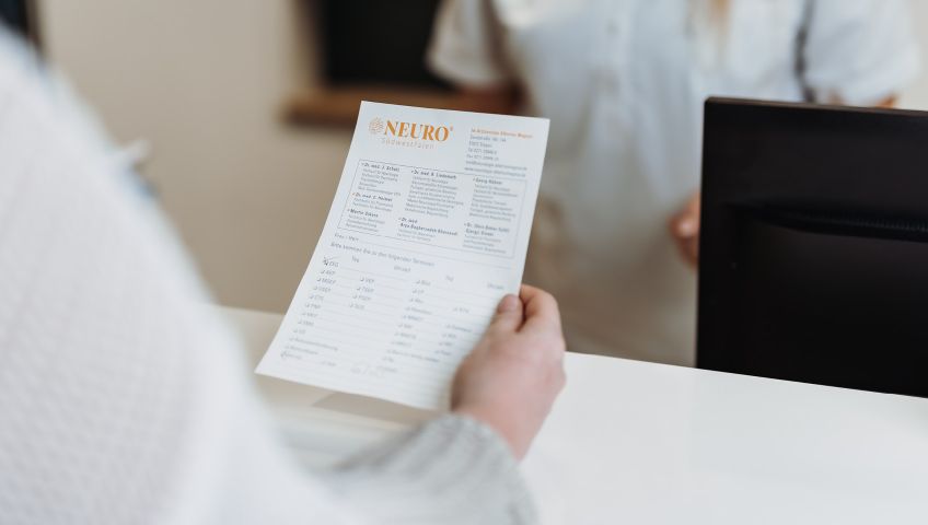 Eine Person blickt auf einen Termin-Zettel von NEURO Südwestfalen in der rechten Hand.