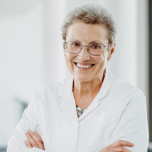 Portraitfoto von Frau Dr. med. Edda Heimel, Fachärztin für Neurologie und Psychiatrie. Sie trägt einen weißen Kittel und lächelt in die Kamera.
