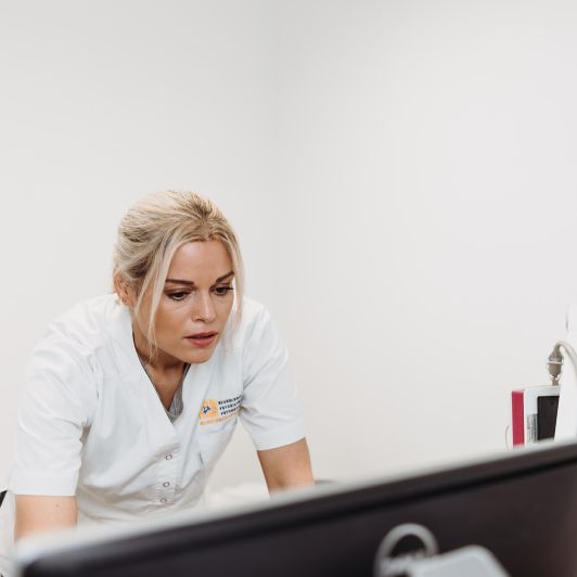 Eine blonde medizinische Fachangestellte in einem weißen Kasack blickt auf einen Monitor
