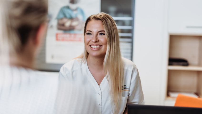 Eine lächelnde, blonde medizinische Fachangestelltevon NEURO Südwestfalen im Gespräch mit einer anderen Person